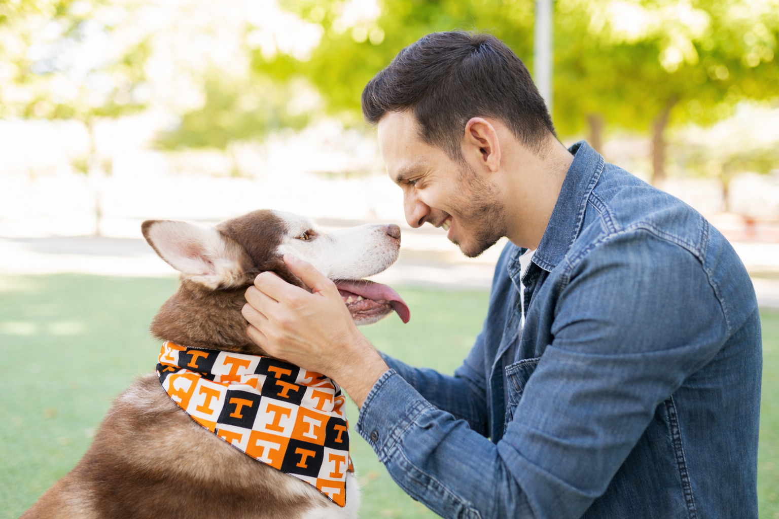 Man petting a dog wearing a bandana with a pattern, outdoors.